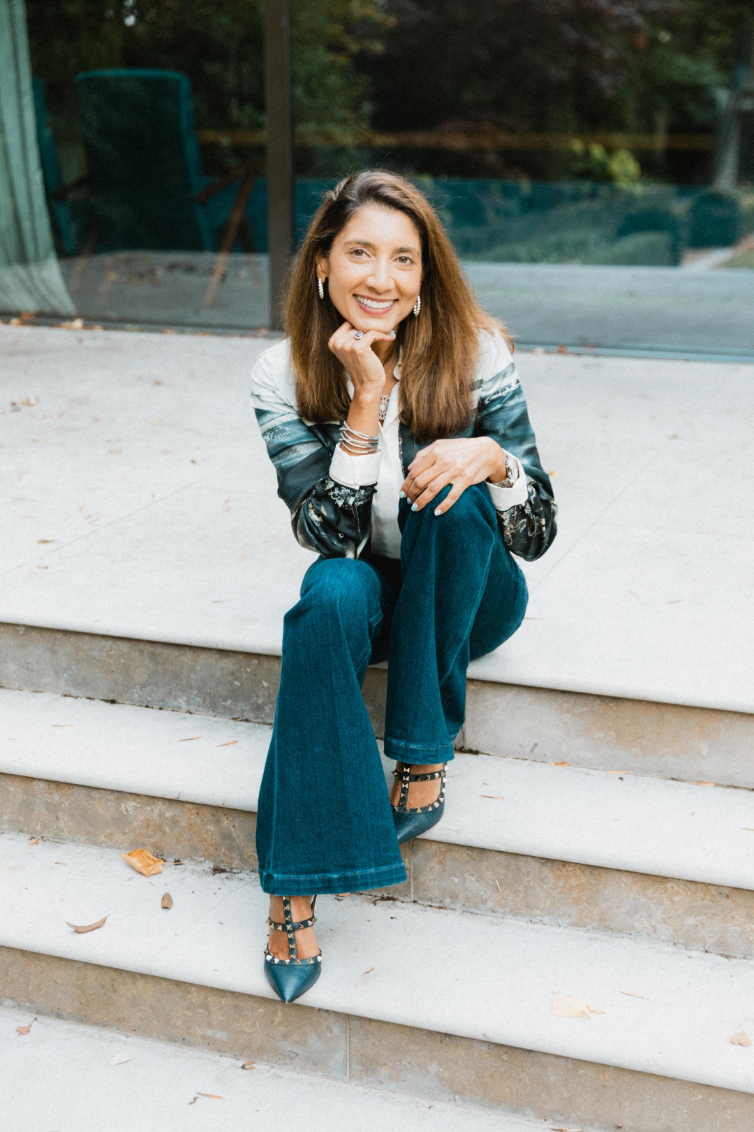 Aliya Kanji seated on stone steps in front of a contemporary glass facade, smiling warmly.